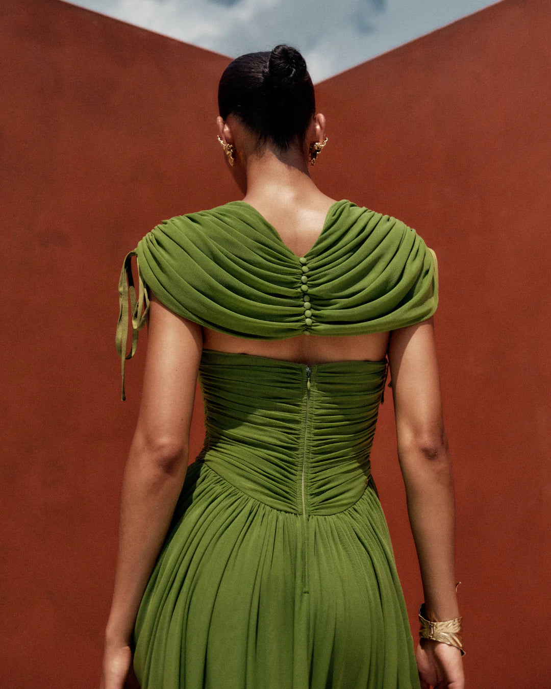 Woman wearing a green dress with a textured back against a red wall
