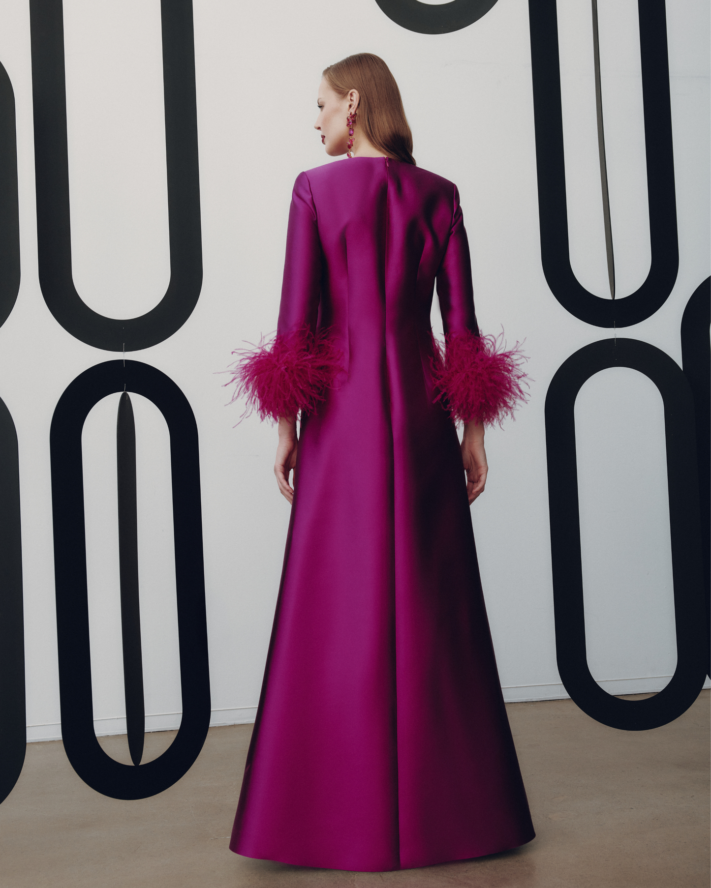 Woman wearing a vibrant pink dress with feathered sleeves against a geometric patterned wall.