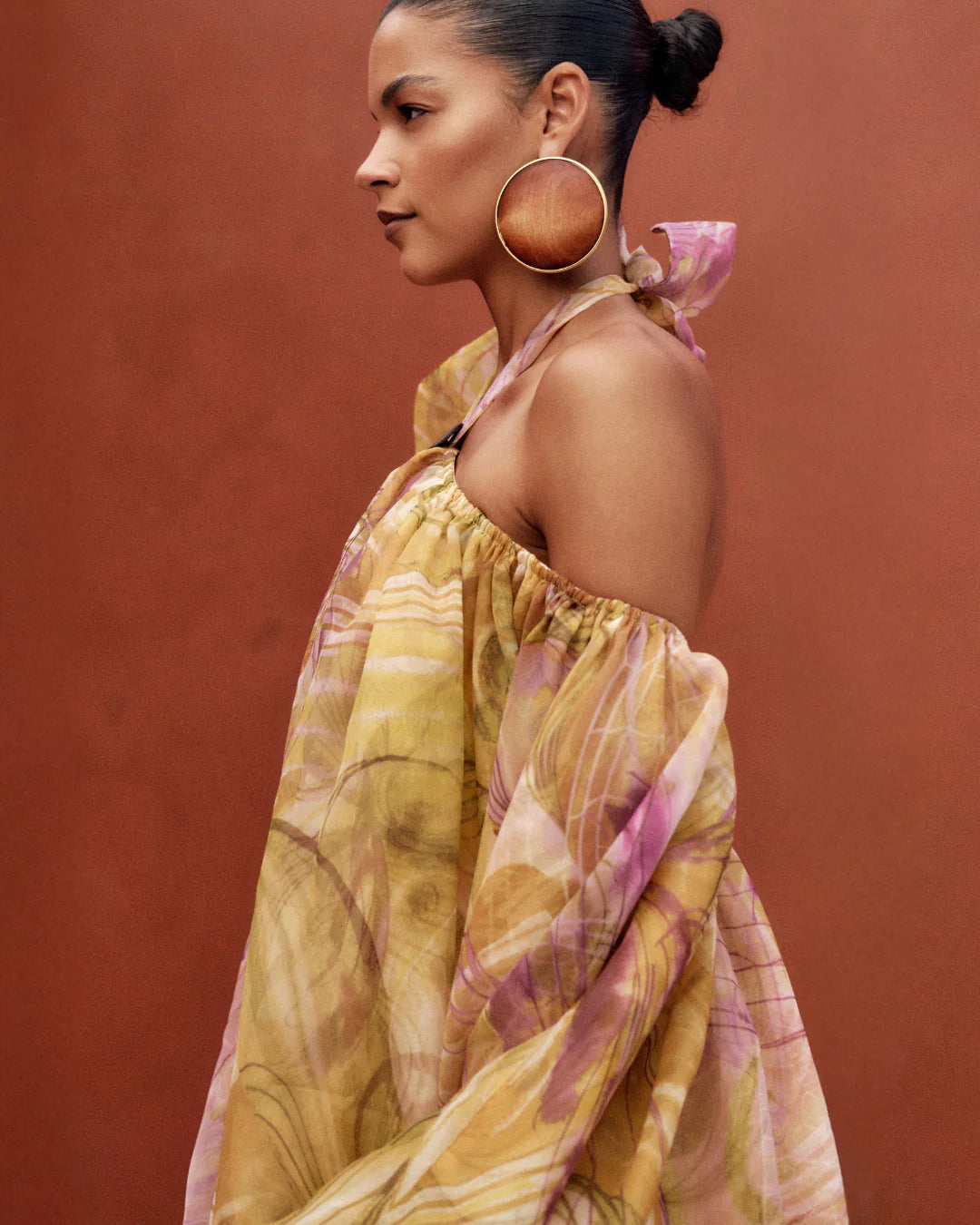 Woman wearing a yellow and pink patterned dress with large earrings against a red background