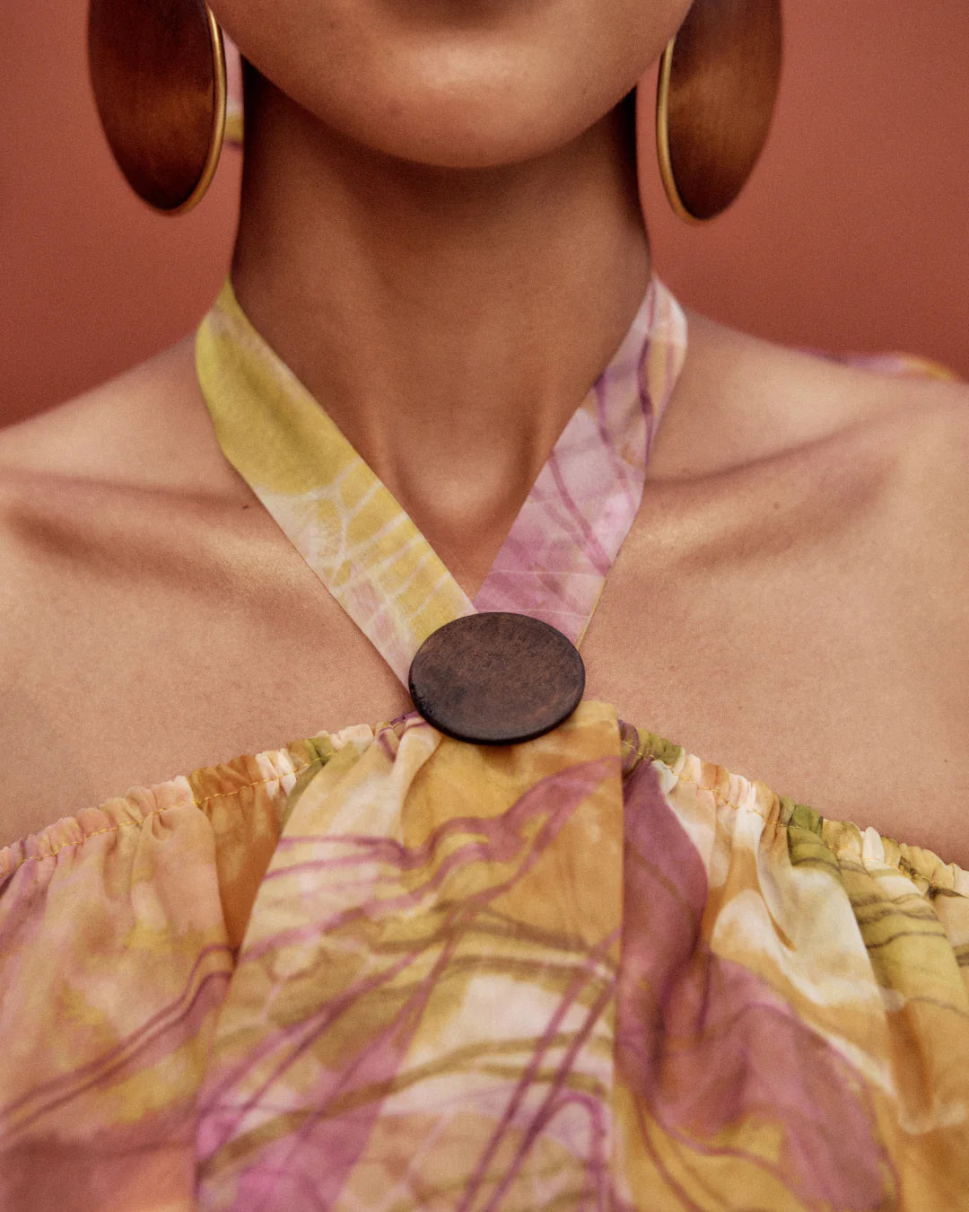 Close-up of a colorful dress with a large wooden button and matching earrings against a brown background.