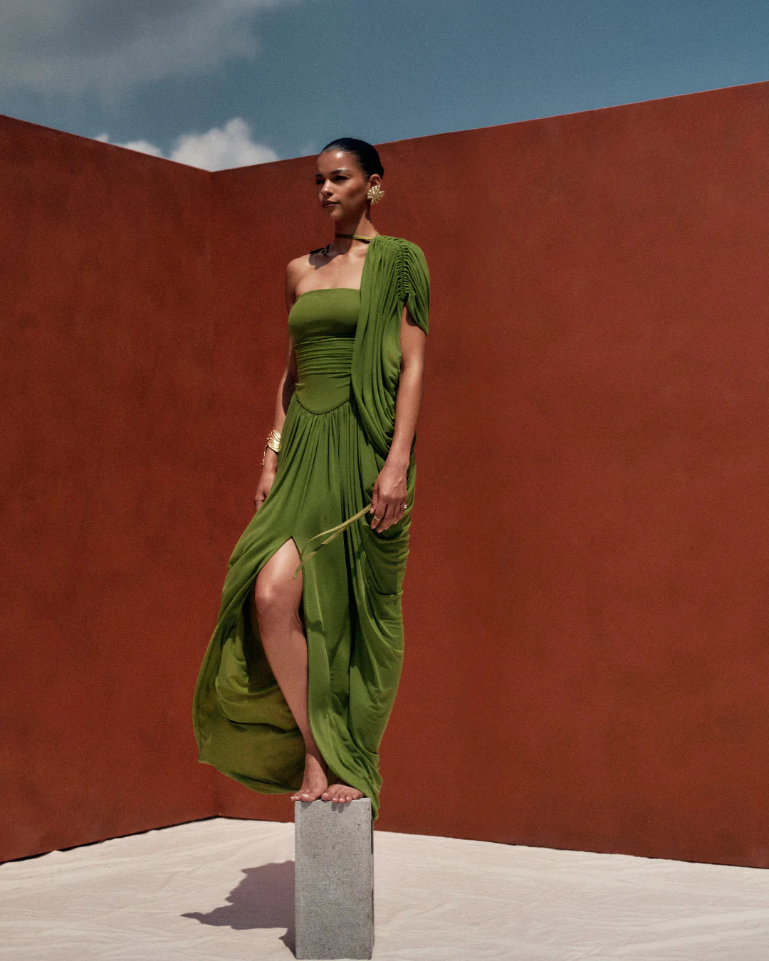 Woman in a green dress standing on a pedestal against a red wall