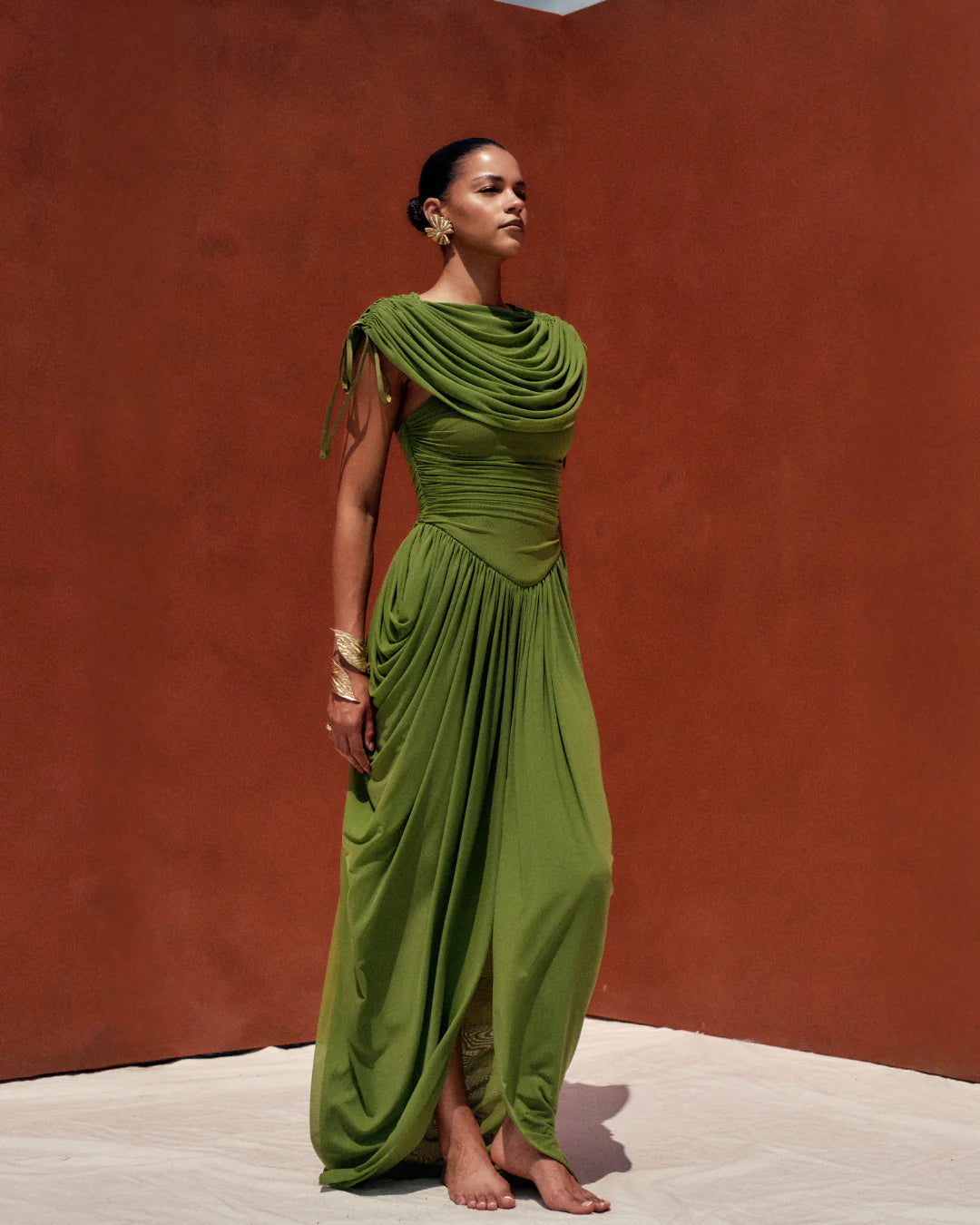 Woman wearing a green evening gown against a red-brown wall.