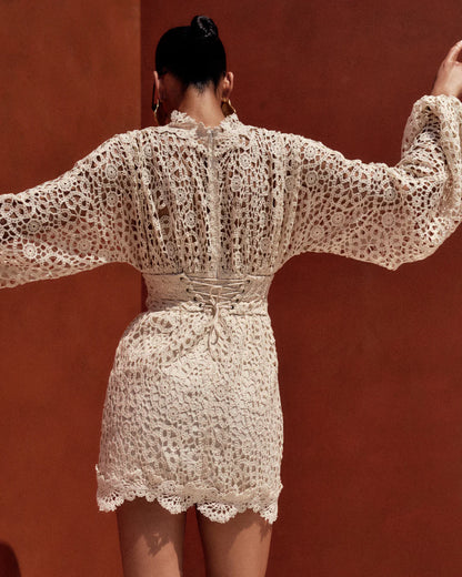 Woman wearing a white lace outfit against a red-brown wall