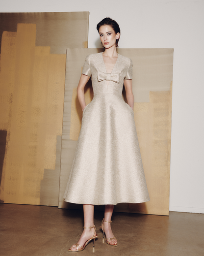 Woman wearing a beige dress with a bow detail in front of abstract art.