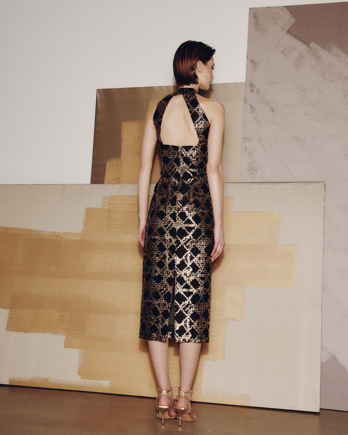 Woman in a black and gold dress standing in front of abstract art