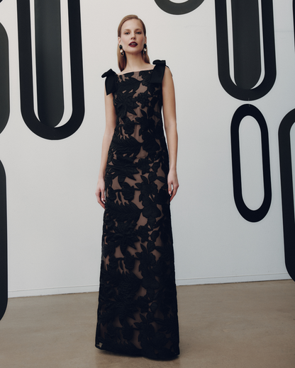 Woman in a black lace dress standing against a white background with large black letters.