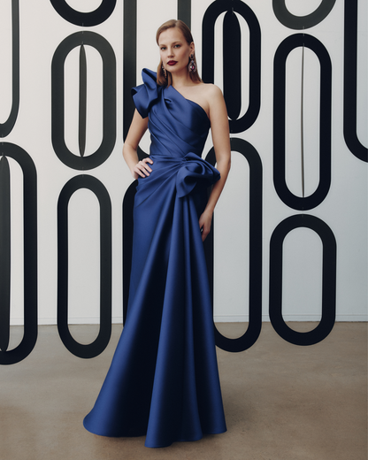 Woman in a blue evening gown standing against a geometric-patterned wall.