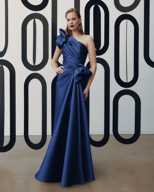 Woman in a blue evening gown standing against a geometric-patterned wall.