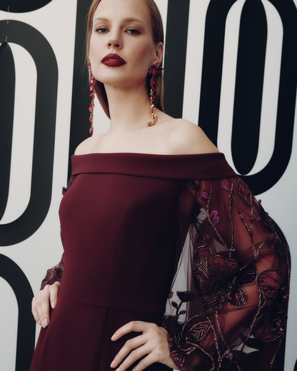 Woman in a burgundy off-shoulder dress with floral details against a black and white patterned background.