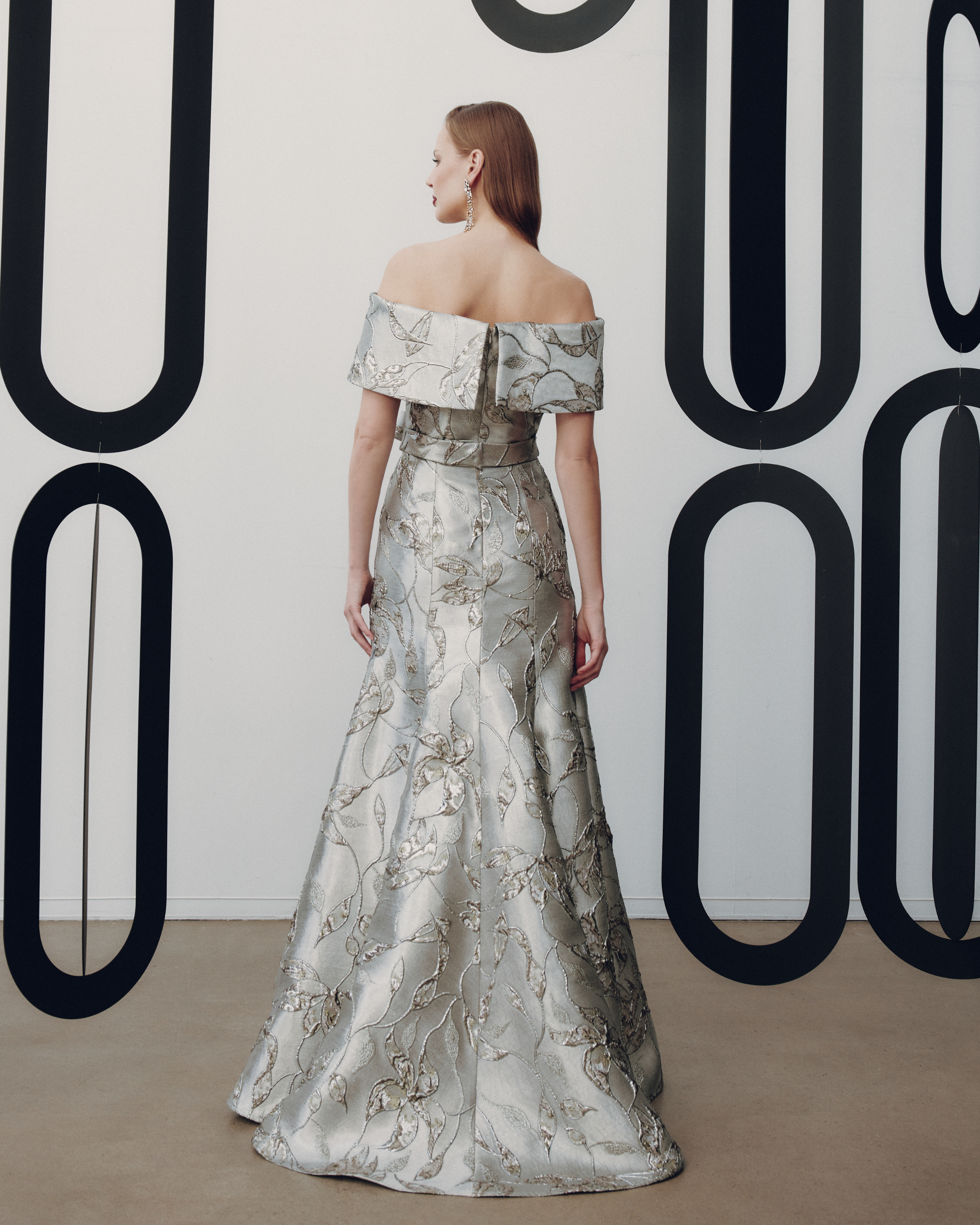 Woman in an off-shoulder floral gown standing against a decorative wall.