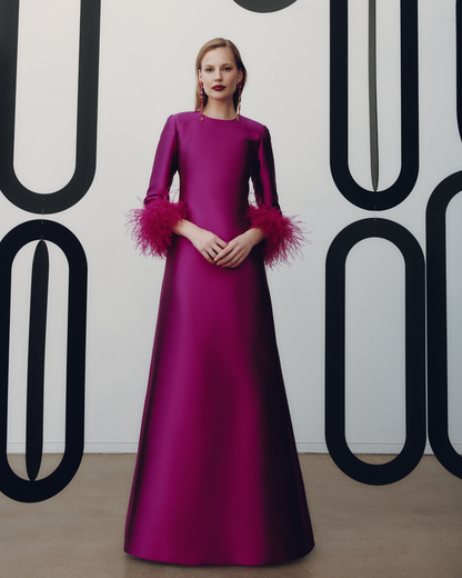 Woman wearing a magenta evening gown with feathered sleeves against a white background with black abstract patterns.
