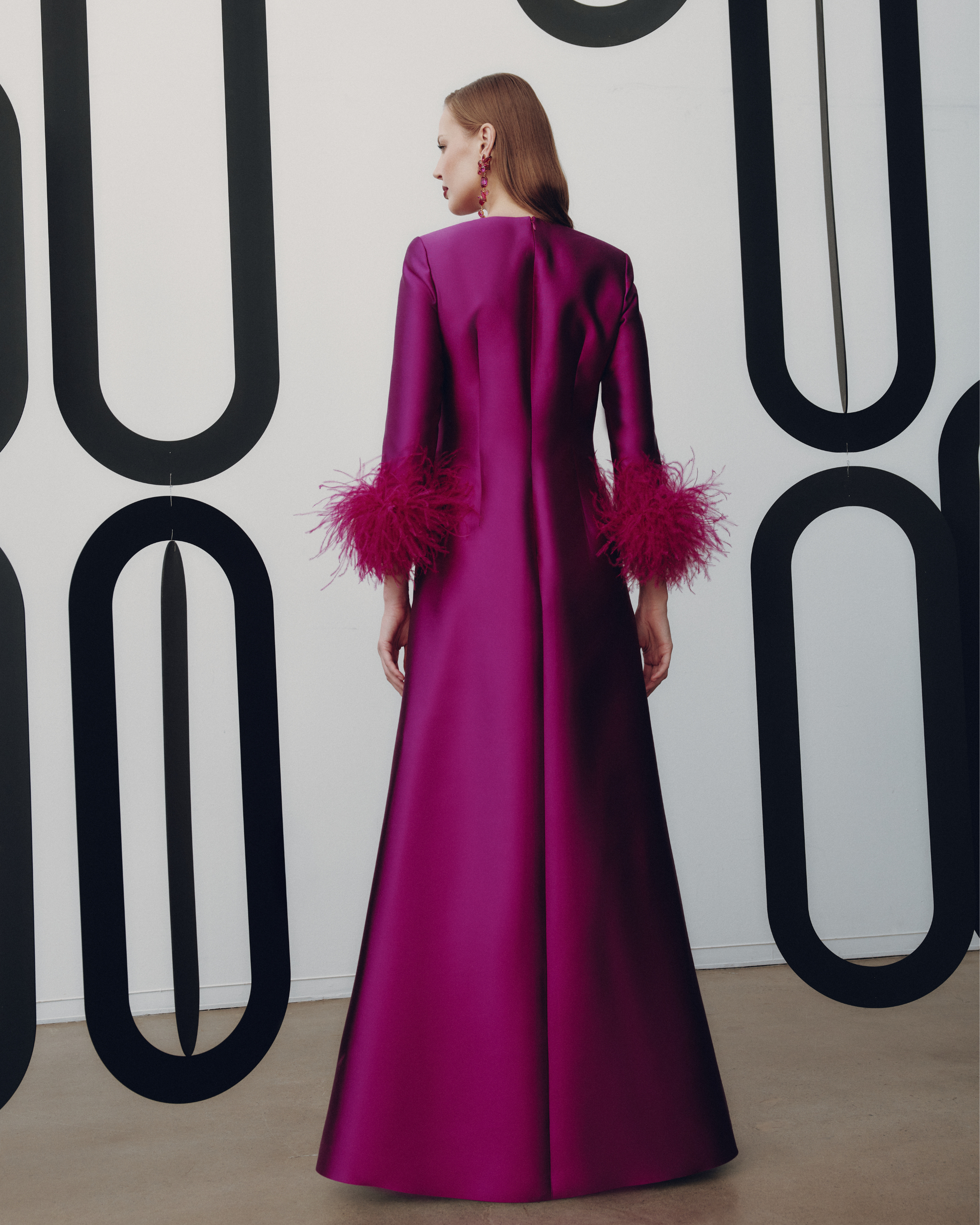 Woman wearing a vibrant pink dress with feathered sleeves against a geometric patterned wall.