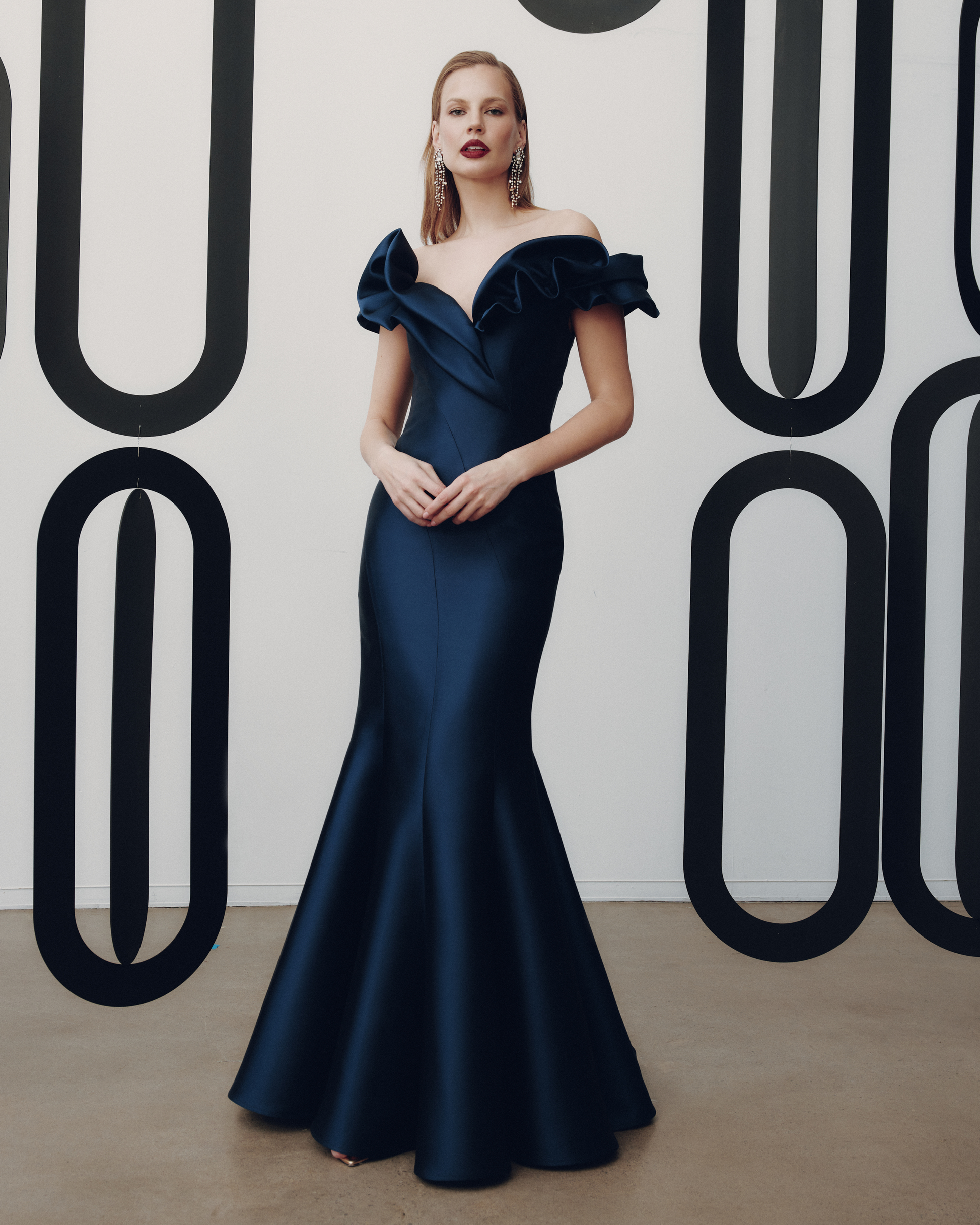 Woman in a navy blue off-shoulder gown against a decorative wall.