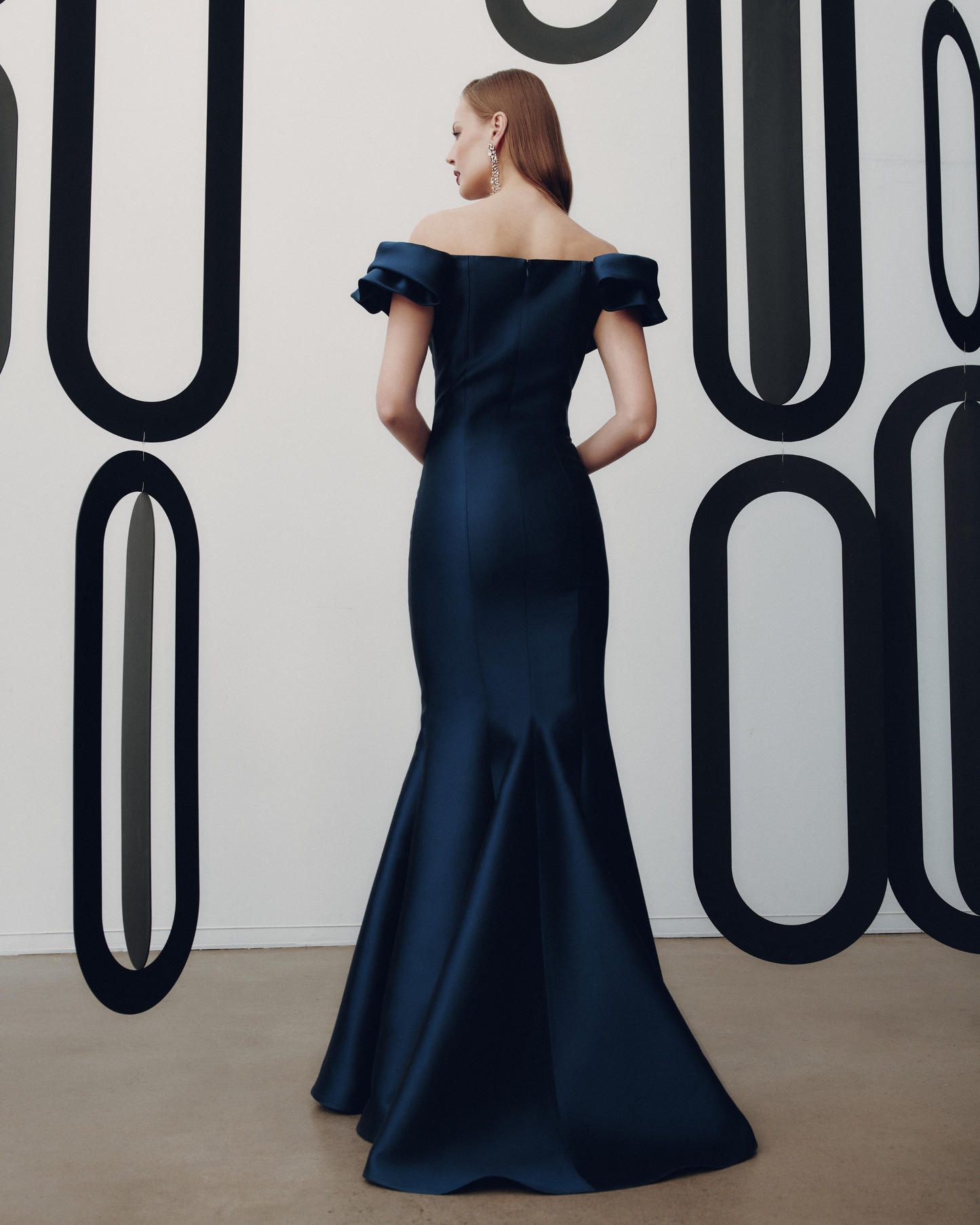 Woman in a navy off-shoulder gown standing against a wall with large black lettering.