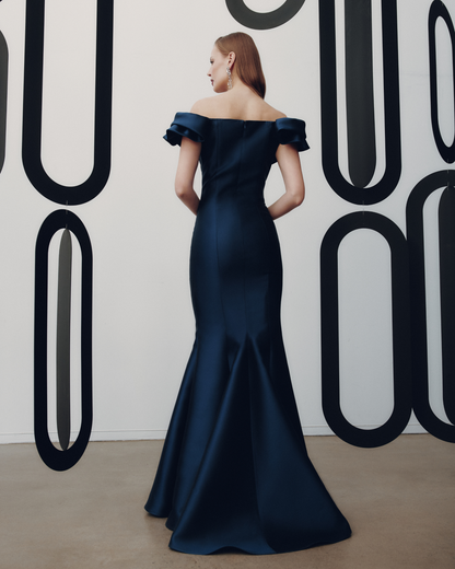 Woman in a navy off-shoulder gown standing against a wall with large black lettering.