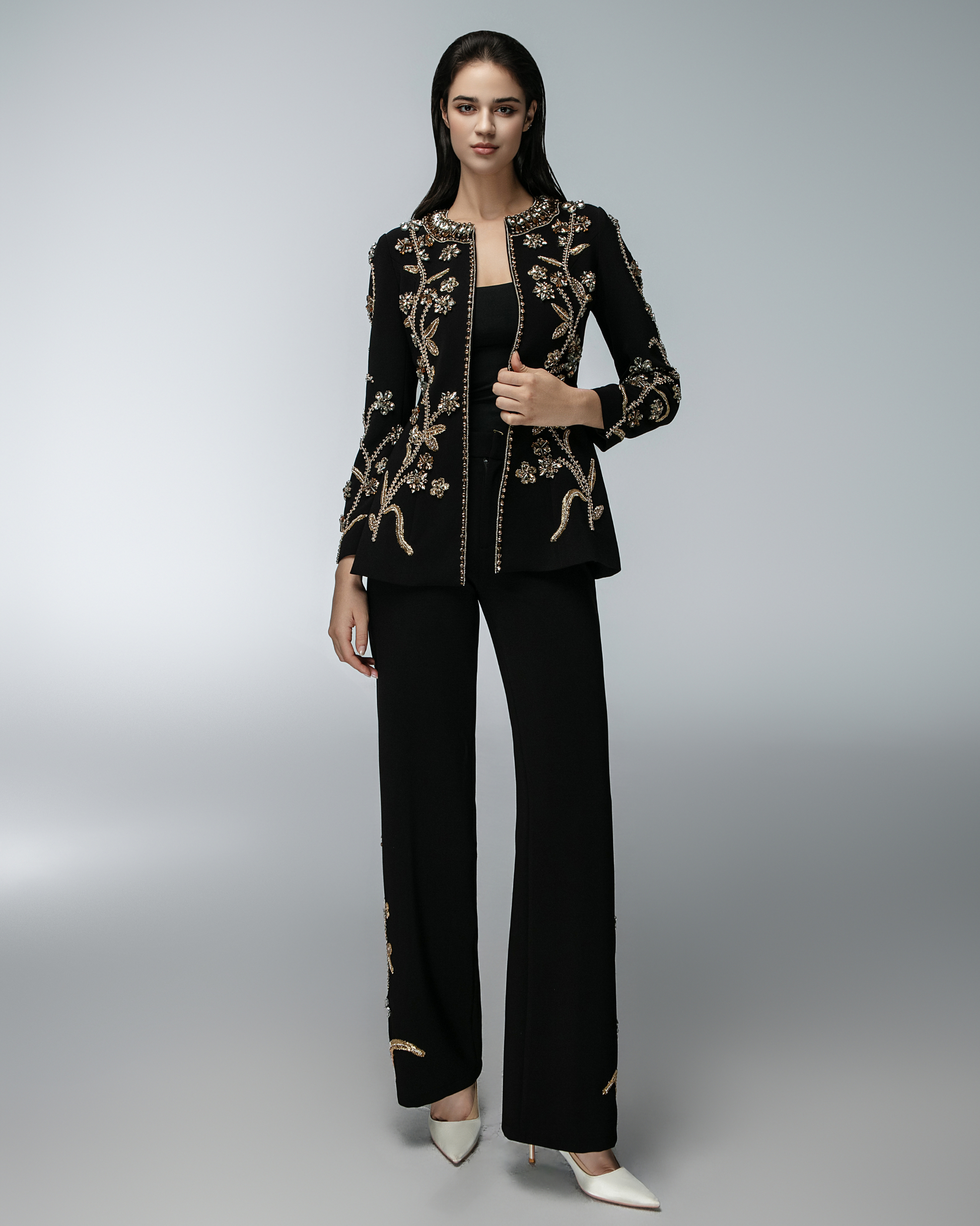 Woman wearing a black embroidered jacket and pants on a gray background