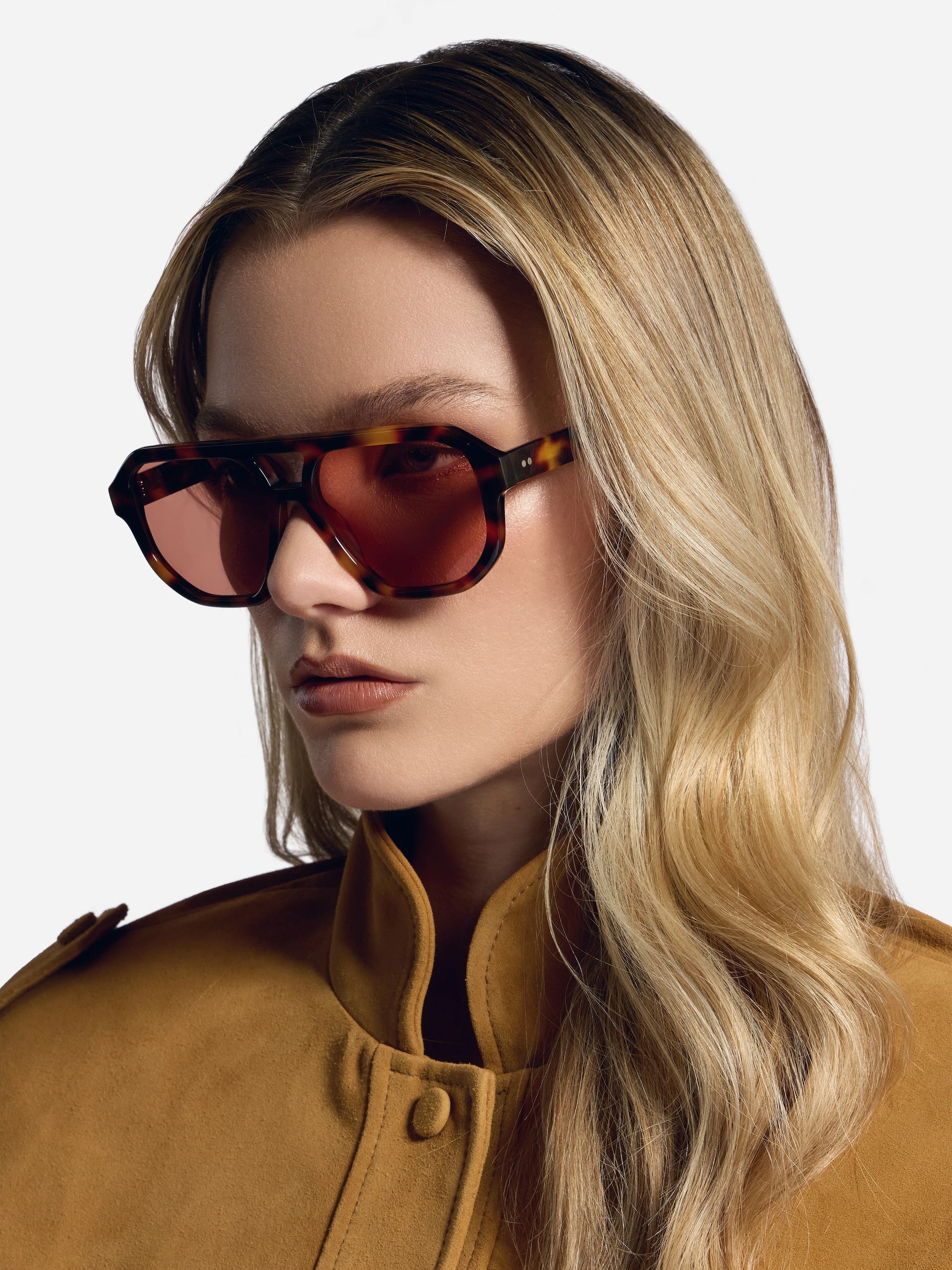 Woman wearing sunglasses and a brown coat against a white background