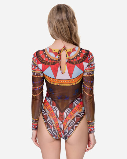 Designer long-sleeve one-piece swimsuit with a sheer mesh base and an intricate, colorful tribal-inspired geometric print featuring orange, red, yellow, black, and white patterns | RODA