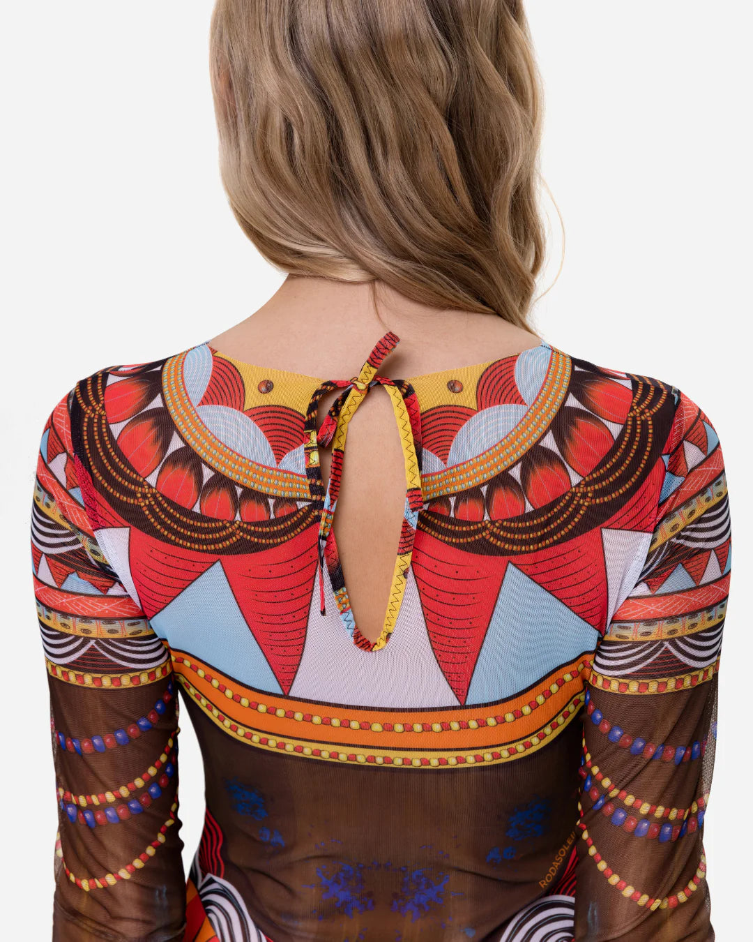 Designer long-sleeve one-piece swimsuit with a sheer mesh base and an intricate, colorful tribal-inspired geometric print featuring orange, red, yellow, black, and white patterns | RODA