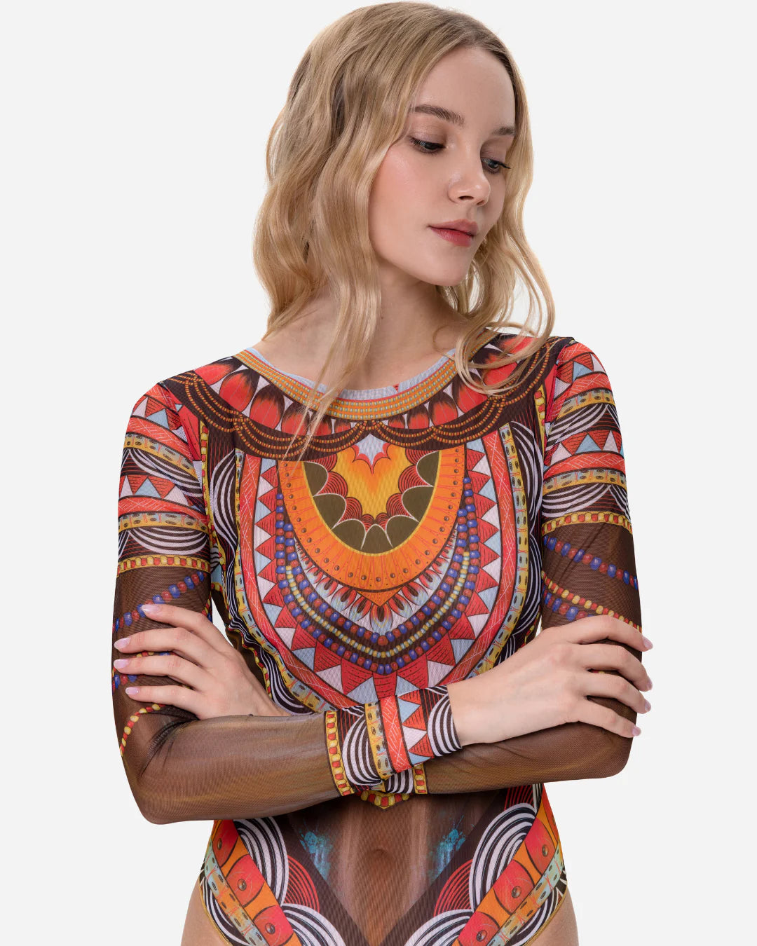 Designer long-sleeve one-piece swimsuit with a sheer mesh base and an intricate, colorful tribal-inspired geometric print featuring orange, red, yellow, black, and white patterns | RODA