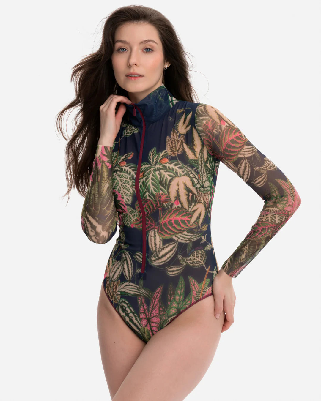 Designer long-sleeve swimsuit with a tropical leaf print in shades of green, pink, and beige over a dark gray base, featuring a dark navy mock neck collar and a dark red front zipper | RODA