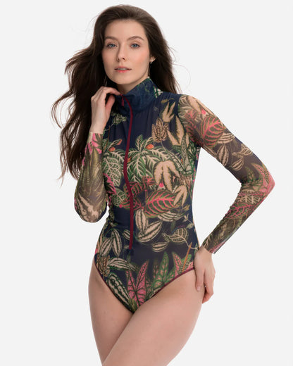 Designer long-sleeve swimsuit with a tropical leaf print in shades of green, pink, and beige over a dark gray base, featuring a dark navy mock neck collar and a dark red front zipper | RODA