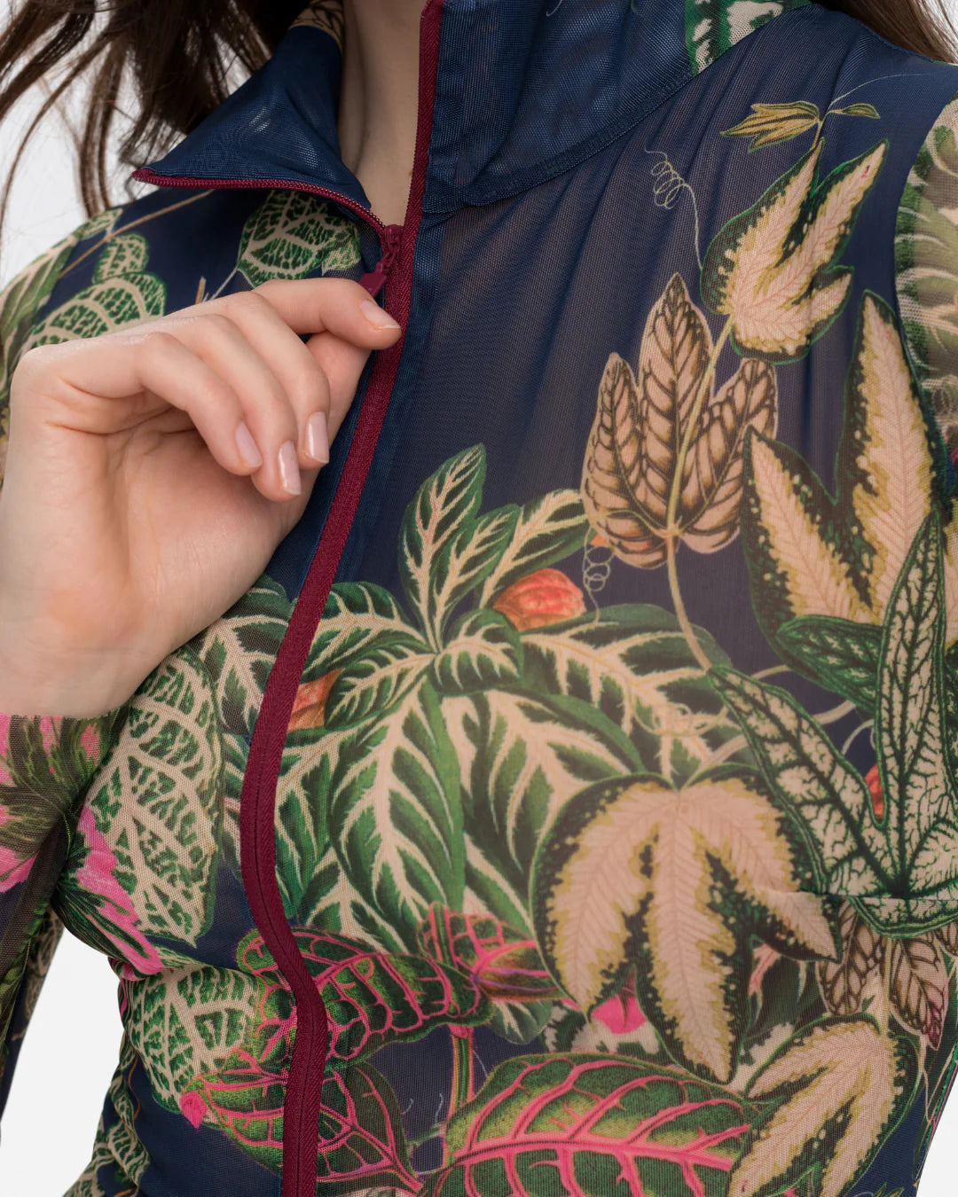 Designer long-sleeve swimsuit with a tropical leaf print in shades of green, pink, and beige over a dark gray base, featuring a dark navy mock neck collar and a dark red front zipper | RODA