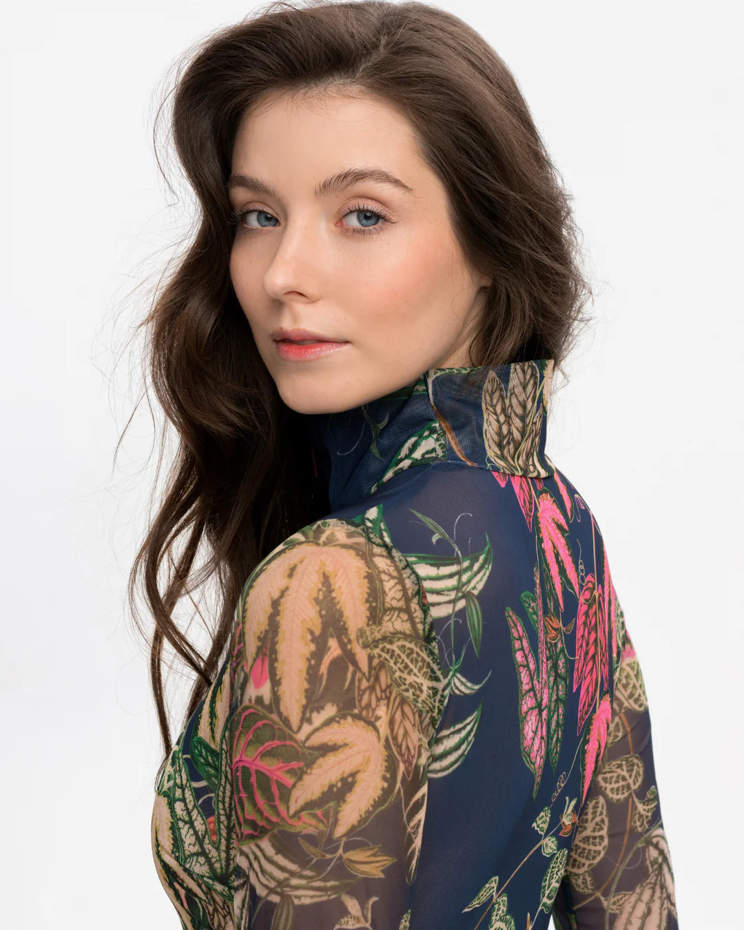 Designer long-sleeve swimsuit with a tropical leaf print in shades of green, pink, and beige over a dark gray base, featuring a dark navy mock neck collar and a dark red front zipper | RODA