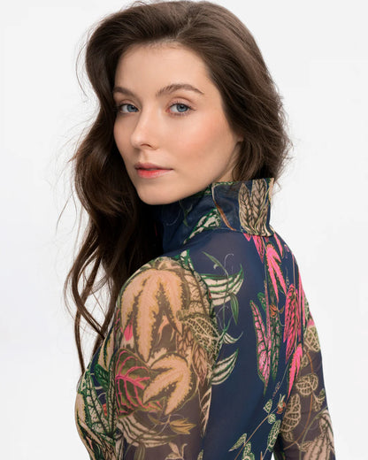 Designer long-sleeve swimsuit with a tropical leaf print in shades of green, pink, and beige over a dark gray base, featuring a dark navy mock neck collar and a dark red front zipper | RODA